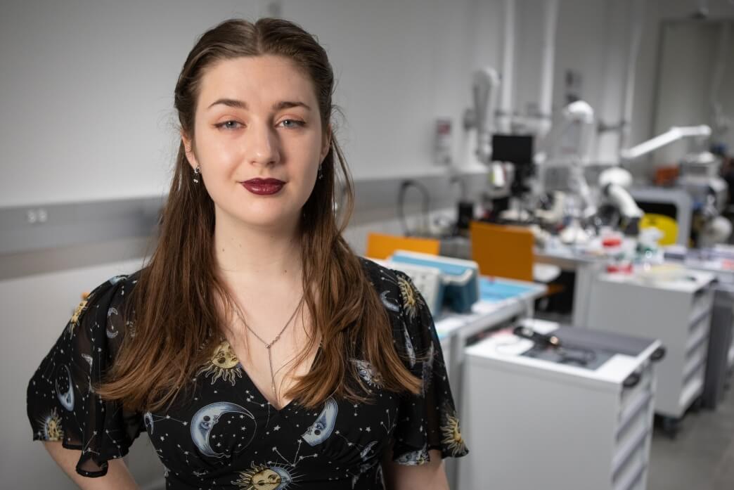 Harvard SEAS senior Molly Boswroth wearing a black shirt with moons, suns and stars, in front of electrical engineering equipment